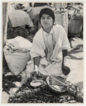 <span itemprop="name">A woman vendor, wearing a white tunic, sitting...</span>