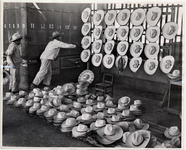<span itemprop="name">Two men standing next to hats laid out and hung up...</span>
