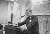 <span itemprop="name">An unidentified man speaking from the podium...</span>