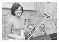 <span itemprop="name">An unidentified woman standing behind a podium...</span>