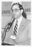 <span itemprop="name">Tom Corigliano at a podium speaking during the...</span>