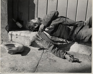 <span itemprop="name">A man lying on a curb against a wall, with a...</span>
